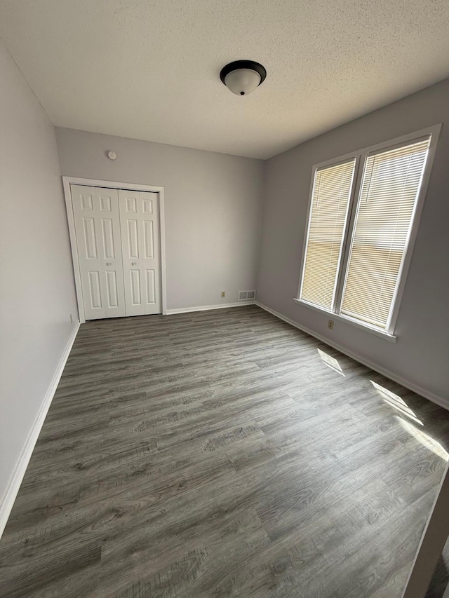 unfurnished bedroom featuring a textured ceiling, a closet, dark wood finished floors, baseboards, and visible vents