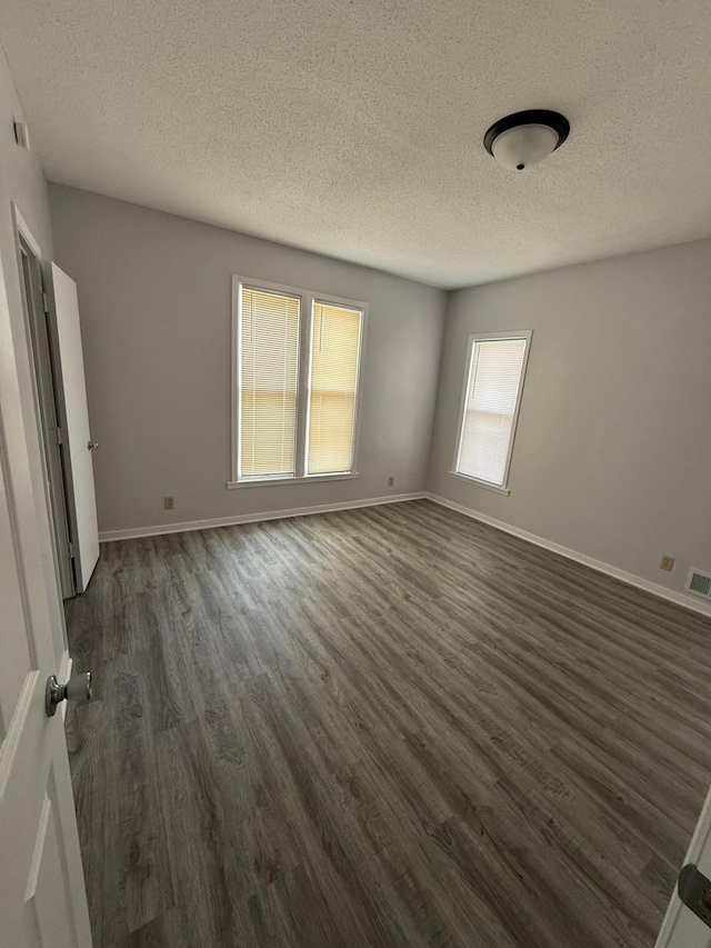 empty room featuring baseboards, visible vents, a textured ceiling, and dark wood finished floors