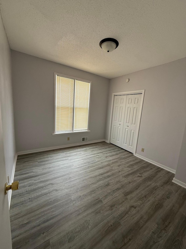 unfurnished bedroom featuring visible vents, a textured ceiling, a closet, and dark wood-style flooring