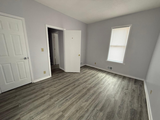unfurnished bedroom with dark wood finished floors, vaulted ceiling, visible vents, and baseboards