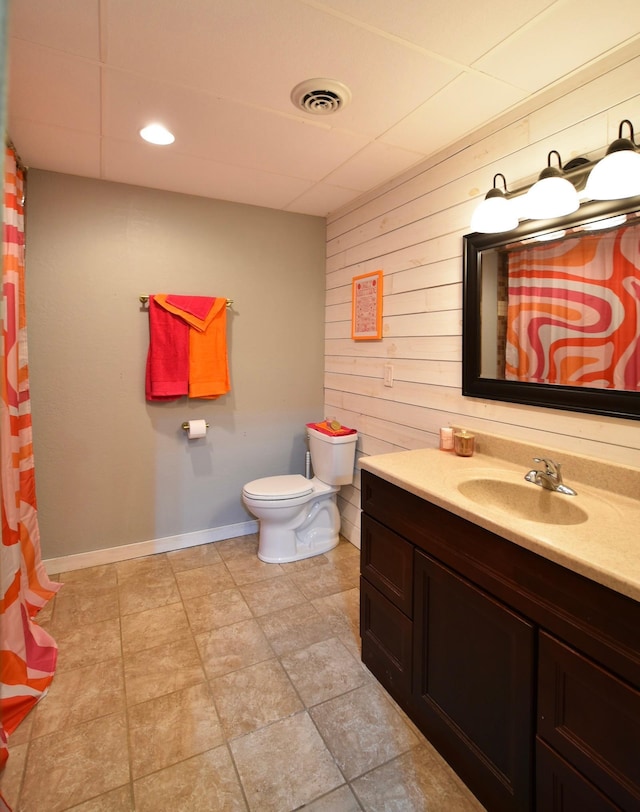 full bathroom featuring toilet, vanity, baseboards, visible vents, and wooden walls