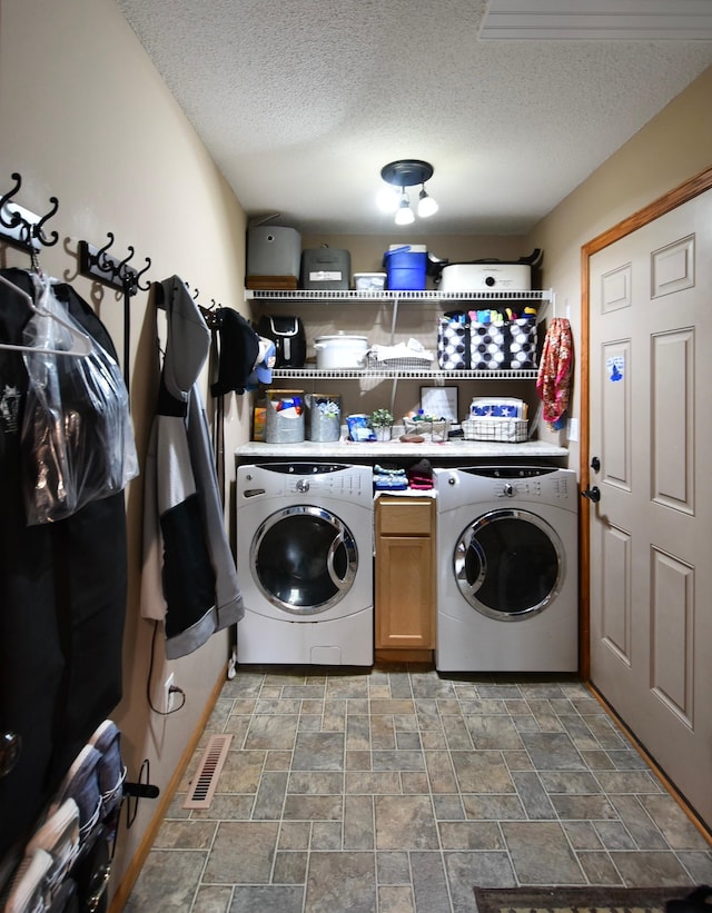 laundry room with stone finish floor, washer and dryer, cabinet space, and a textured ceiling