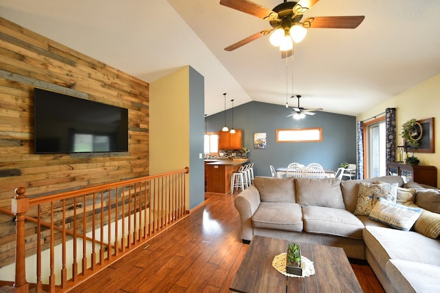 living area with wood walls, hardwood / wood-style flooring, a ceiling fan, and vaulted ceiling