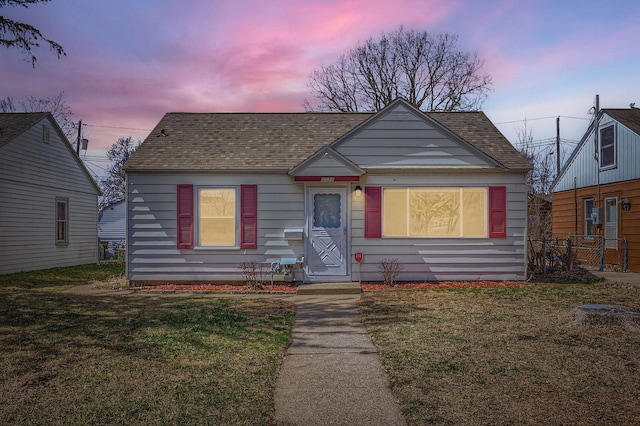 bungalow-style home with a lawn, fence, and roof with shingles