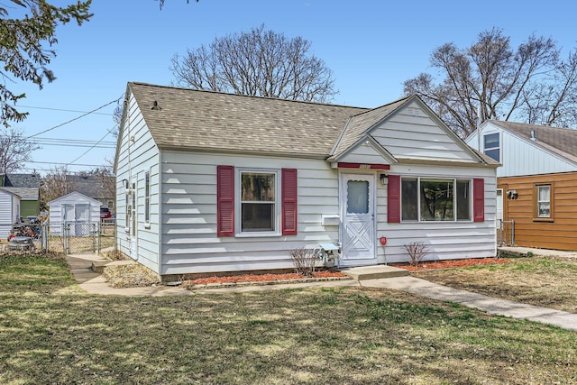 bungalow-style house with a storage shed, an outbuilding, a front lawn, fence, and a shingled roof