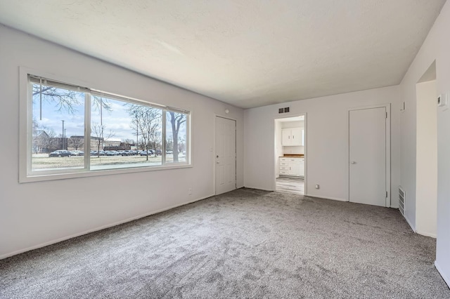 unfurnished bedroom with ensuite bath, carpet floors, visible vents, and baseboards