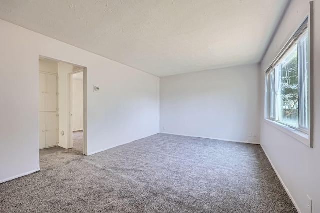 carpeted spare room featuring a textured ceiling and baseboards
