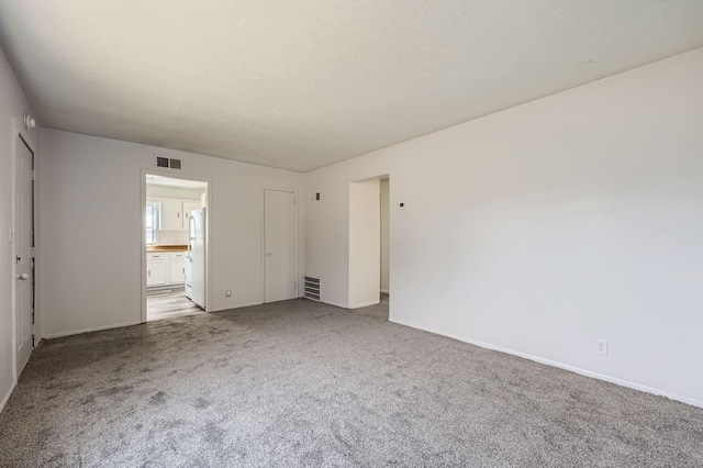 interior space featuring visible vents, baseboards, freestanding refrigerator, and carpet flooring