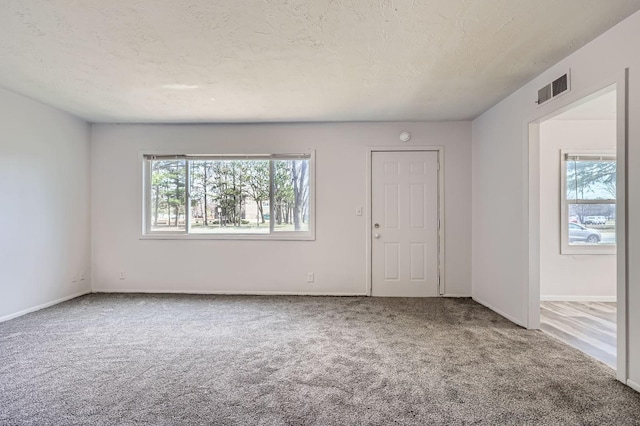 unfurnished room with baseboards, a textured ceiling, visible vents, and carpet