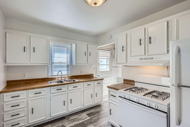 kitchen featuring wood finished floors, a sink, under cabinet range hood, white appliances, and white cabinetry