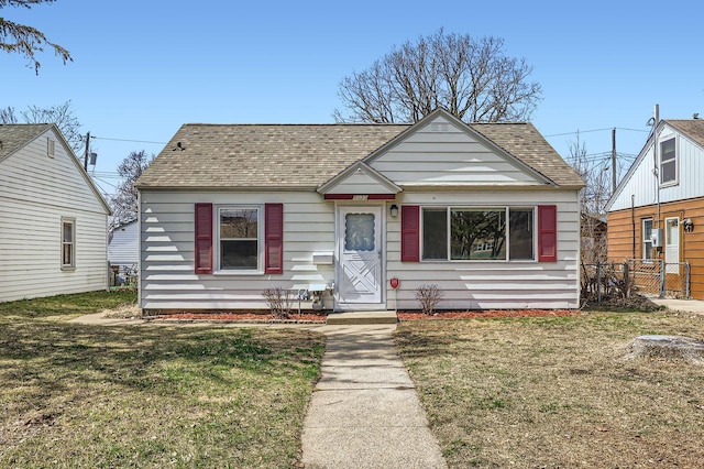bungalow with roof with shingles, a front lawn, and fence