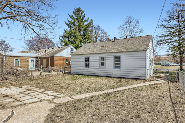 back of property with a gate, a yard, roof with shingles, and a fenced backyard