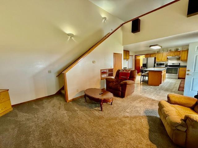 living area featuring baseboards, high vaulted ceiling, stairs, and light carpet