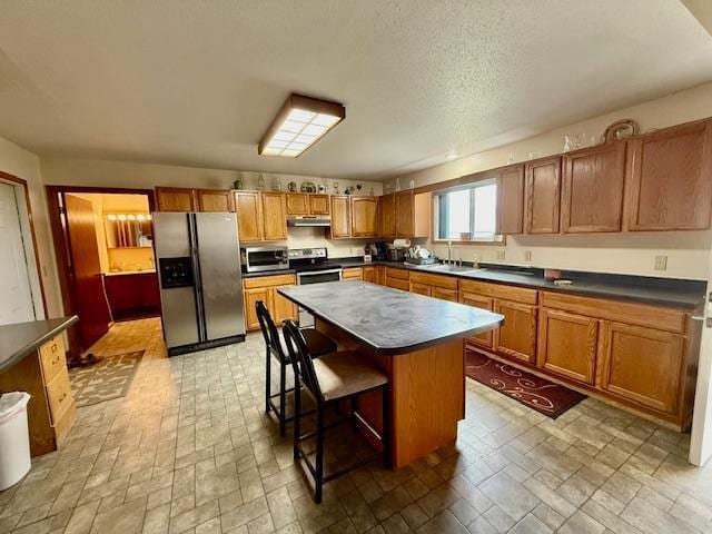kitchen featuring a sink, stainless steel appliances, under cabinet range hood, a center island, and dark countertops