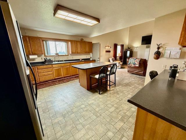 kitchen featuring a kitchen breakfast bar, a kitchen island, freestanding refrigerator, open floor plan, and brown cabinetry