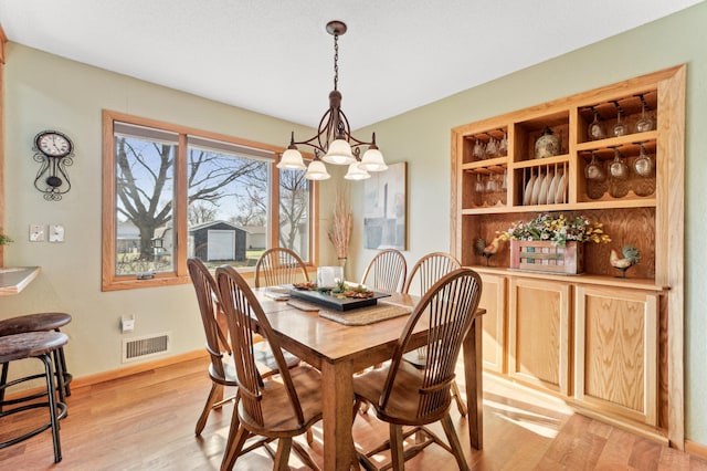 dining space featuring baseboards, an inviting chandelier, visible vents, and light wood-style flooring