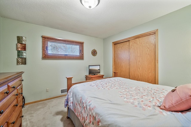 bedroom featuring a textured ceiling, baseboards, visible vents, light colored carpet, and a closet