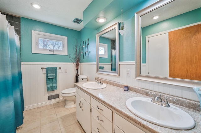 bathroom featuring visible vents, toilet, wainscoting, and a sink