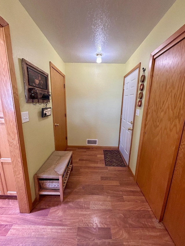 corridor with baseboards, wood finished floors, visible vents, and a textured ceiling