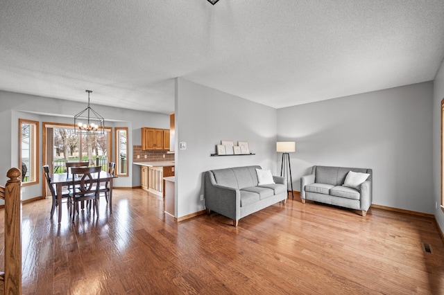 living area with visible vents, a textured ceiling, light wood finished floors, and a notable chandelier