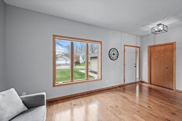 foyer entrance with baseboards, light wood finished floors, a chandelier, and visible vents