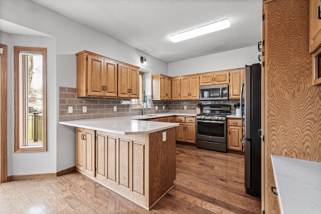 kitchen with decorative backsplash, a peninsula, dark wood-type flooring, light countertops, and appliances with stainless steel finishes
