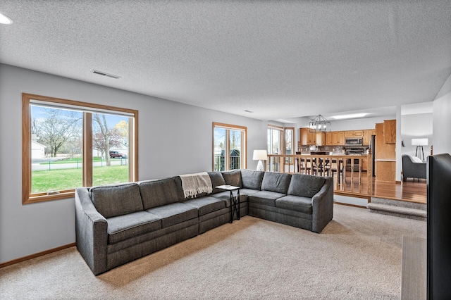 living area with a textured ceiling, a notable chandelier, light colored carpet, and plenty of natural light