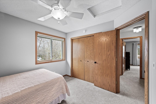 bedroom featuring a textured ceiling, light carpet, attic access, and a closet
