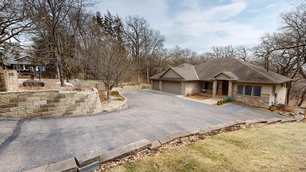 view of front facade featuring an attached garage, stone siding, and aphalt driveway