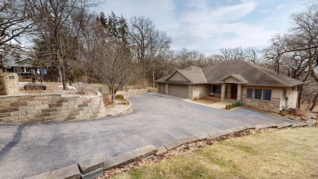 view of front facade featuring an attached garage, stone siding, and aphalt driveway