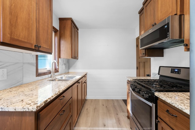 5840 Nevada Ave N, Crystal, MN 55428 - kitchen featuring stainless steel appliances, a sink, light wood-style flooring, a wainscoted wall, and light stone countertops
