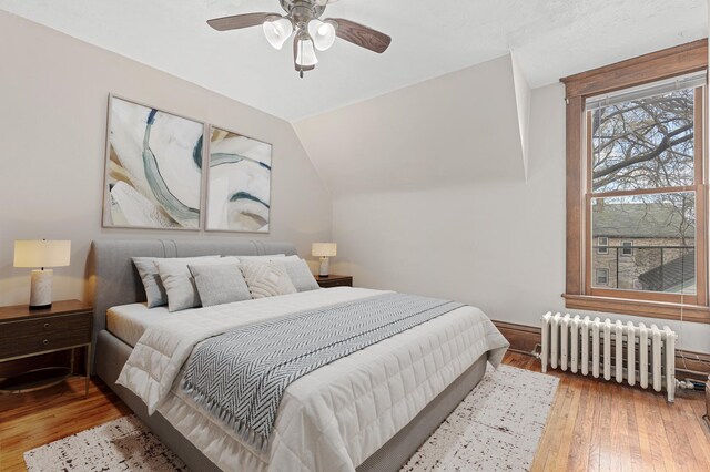 bedroom featuring radiator, hardwood / wood-style floors, a ceiling fan, baseboards, and lofted ceiling