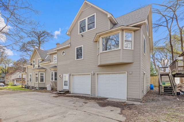 back of house featuring an attached garage, a shingled roof, driveway, and stairway