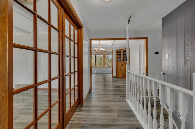 corridor featuring a textured ceiling, french doors, an inviting chandelier, wooden walls, and wood finished floors