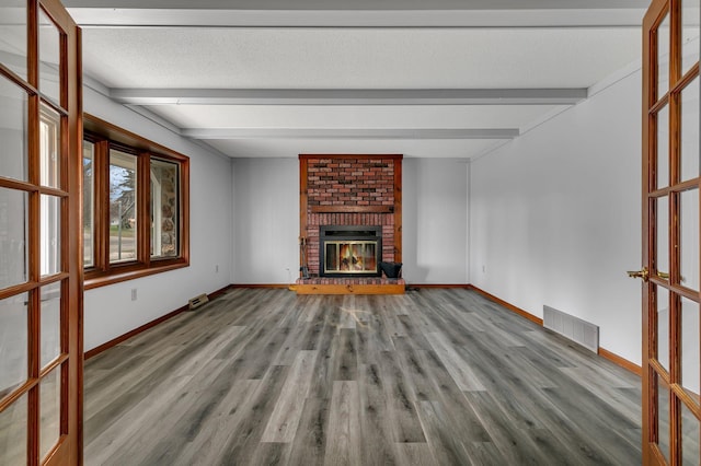 unfurnished living room with wood finished floors, visible vents, beamed ceiling, and baseboards