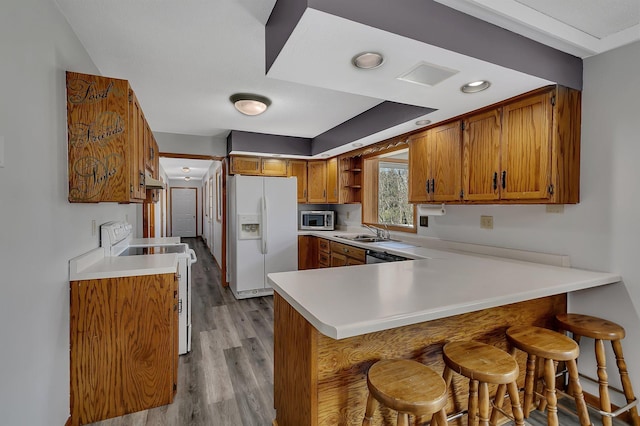 kitchen with a sink, brown cabinets, a peninsula, white appliances, and wood finished floors