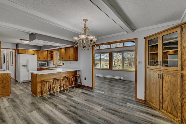 kitchen featuring white refrigerator with ice dispenser, stainless steel microwave, brown cabinetry, baseboard heating, and a peninsula