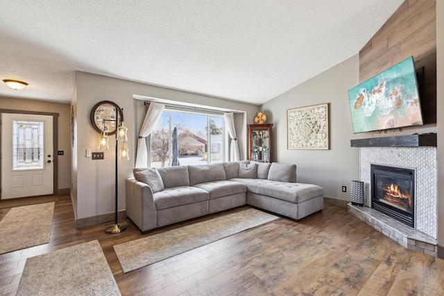 living area with a tile fireplace, wood finished floors, baseboards, a textured ceiling, and lofted ceiling