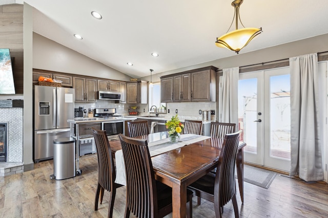 dining area featuring light wood-type flooring, recessed lighting, vaulted ceiling, french doors, and a tiled fireplace