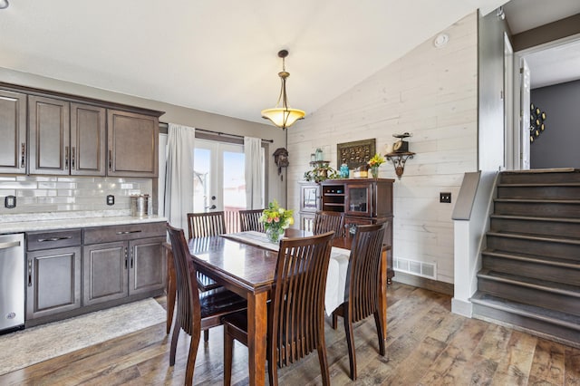 dining room featuring visible vents, wooden walls, light wood-type flooring, vaulted ceiling, and stairs