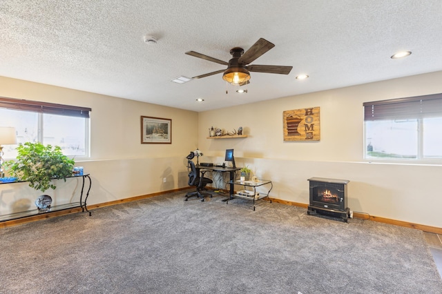 carpeted home office with ceiling fan, a wood stove, and baseboards