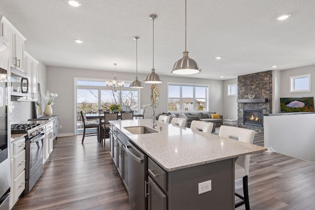 kitchen featuring a textured ceiling, a sink, a breakfast bar area, stainless steel appliances, and a fireplace