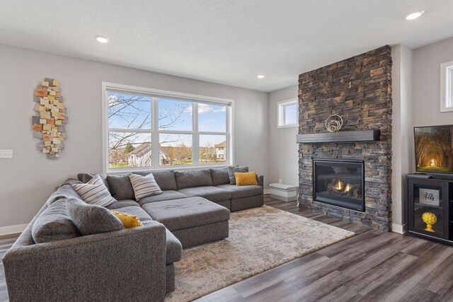 living room featuring baseboards, wood finished floors, a stone fireplace, and recessed lighting