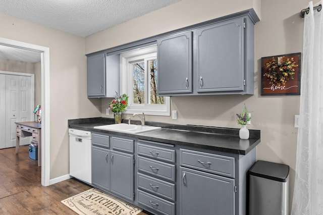 kitchen featuring gray cabinets, a textured ceiling, dark countertops, dishwasher, and a sink