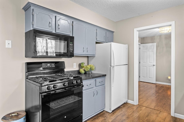 kitchen with dark countertops, a textured ceiling, baseboards, wood finished floors, and black appliances