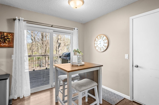 dining space featuring a textured ceiling, baseboards, and wood finished floors