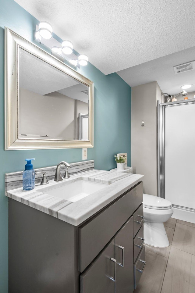 bathroom with a textured ceiling, visible vents, an enclosed shower, vanity, and toilet