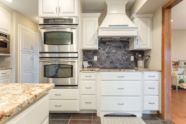 kitchen with white cabinets, double oven, black electric cooktop, tasteful backsplash, and custom exhaust hood