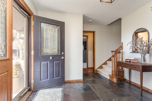 foyer entrance with stairway, baseboards, and stone tile flooring
