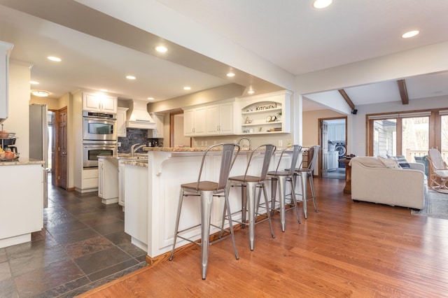 kitchen featuring a peninsula, double oven, a breakfast bar, and custom range hood